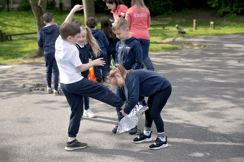 a child almost falling over as another child wraps tin foil around their foot for an experiment