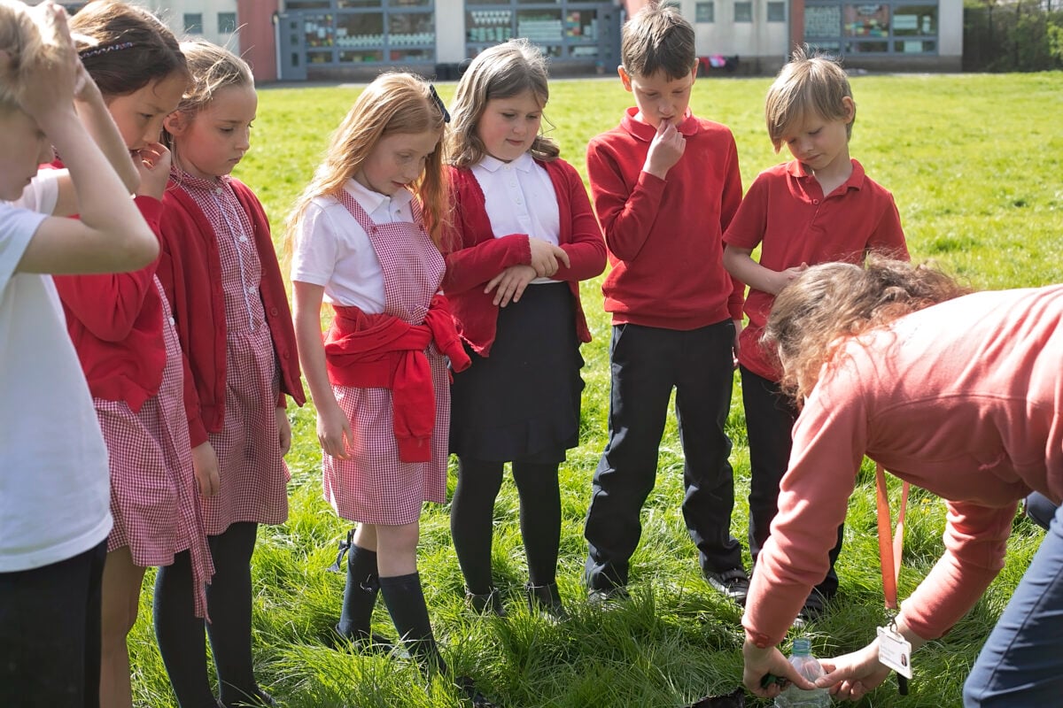 A group of children focusing on an adult demonstrating an outdoor activity