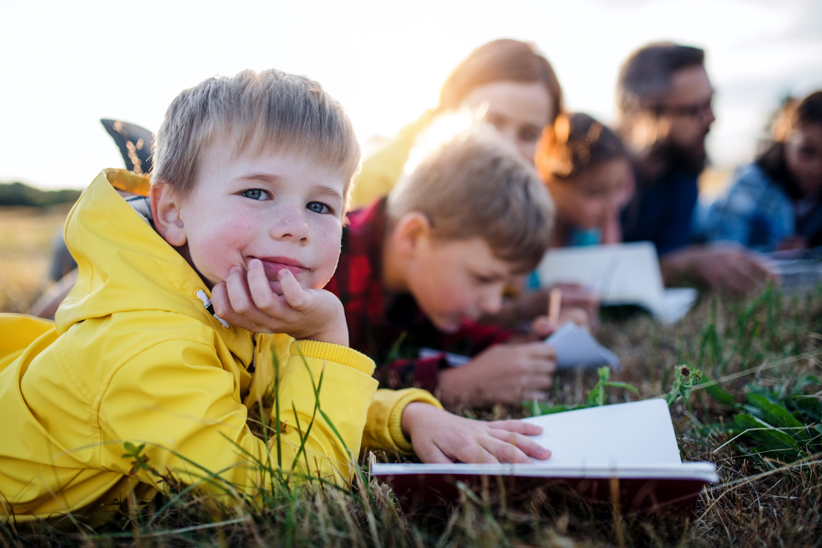 Children learning outdoors, laid down writing in the grass