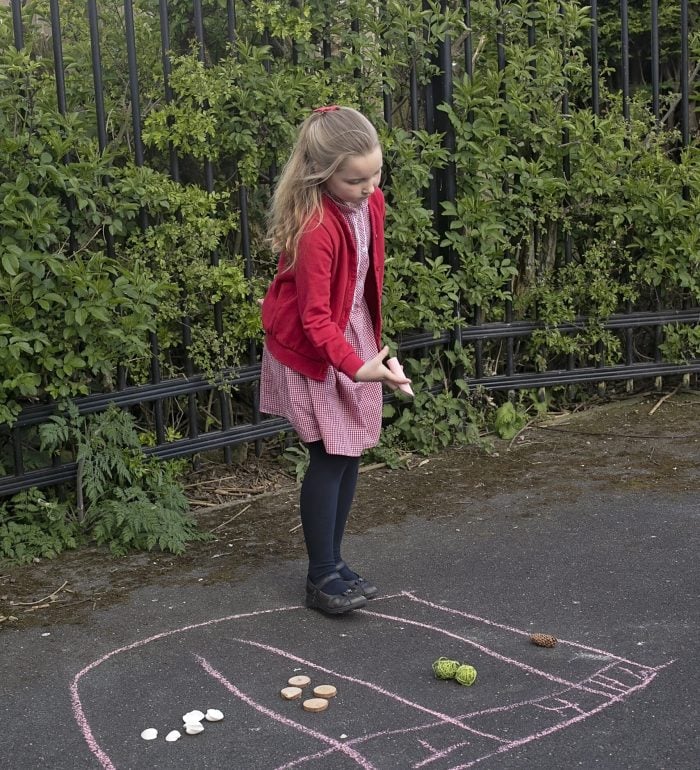 A girl completing a place value table outside on the playground with chalk