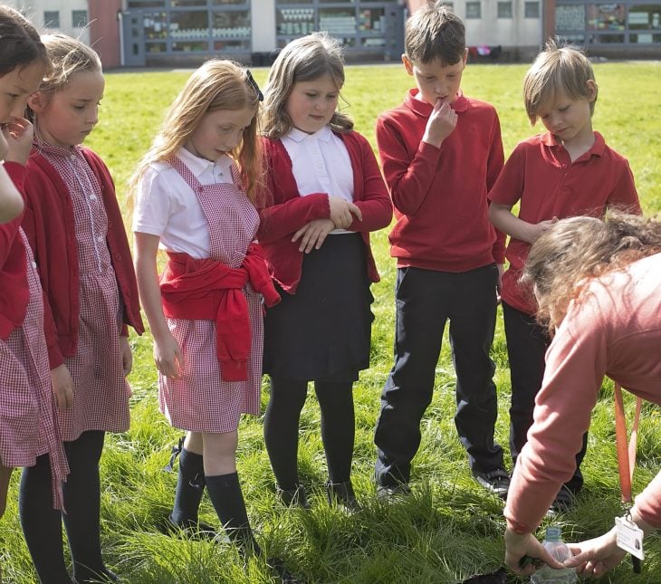 A group of children focusing on an adult demonstrating an outdoor activity
