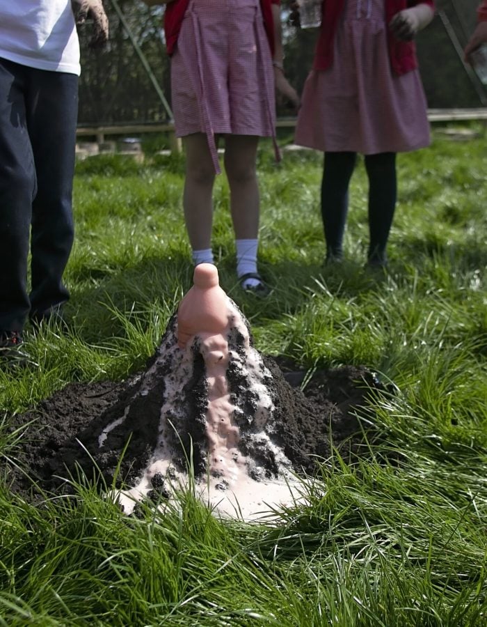 Children watching a volcano constructed of mud erupt with orange foam