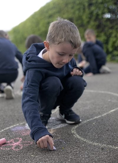 A boy using chalk to spell words phonetically outdoors