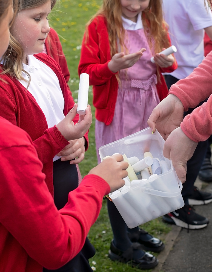 A teacher handing out playground chalk to a group of children