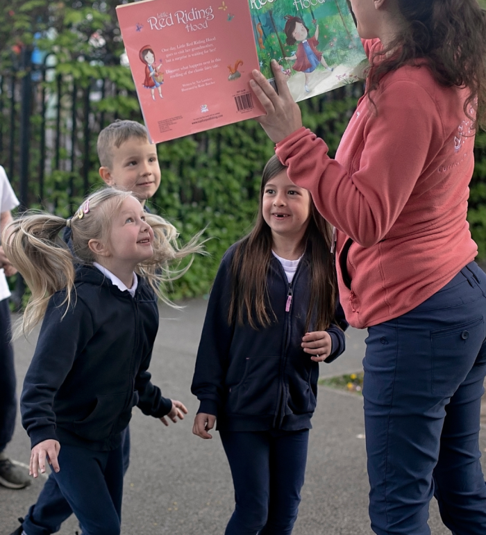 A teacher reading to a class of children outside on the playground