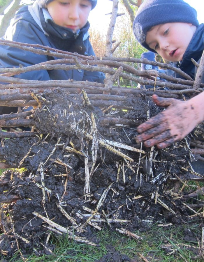 two boys building a wall with sticks and mud