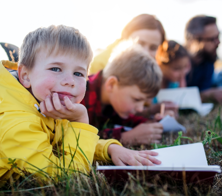 Children learning outdoors, laid down writing in the grass
