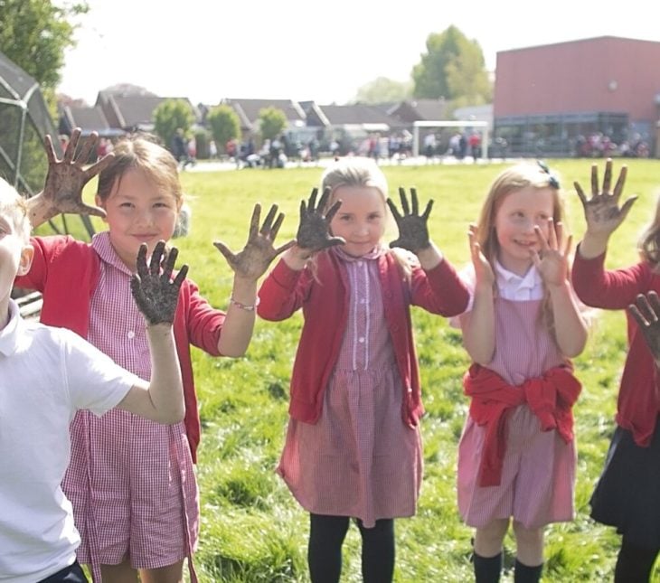A group of children with muddy hands smiling and laughing