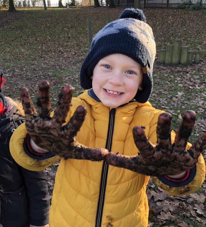A boy in a yellow coat, gleaming with very muddy hands