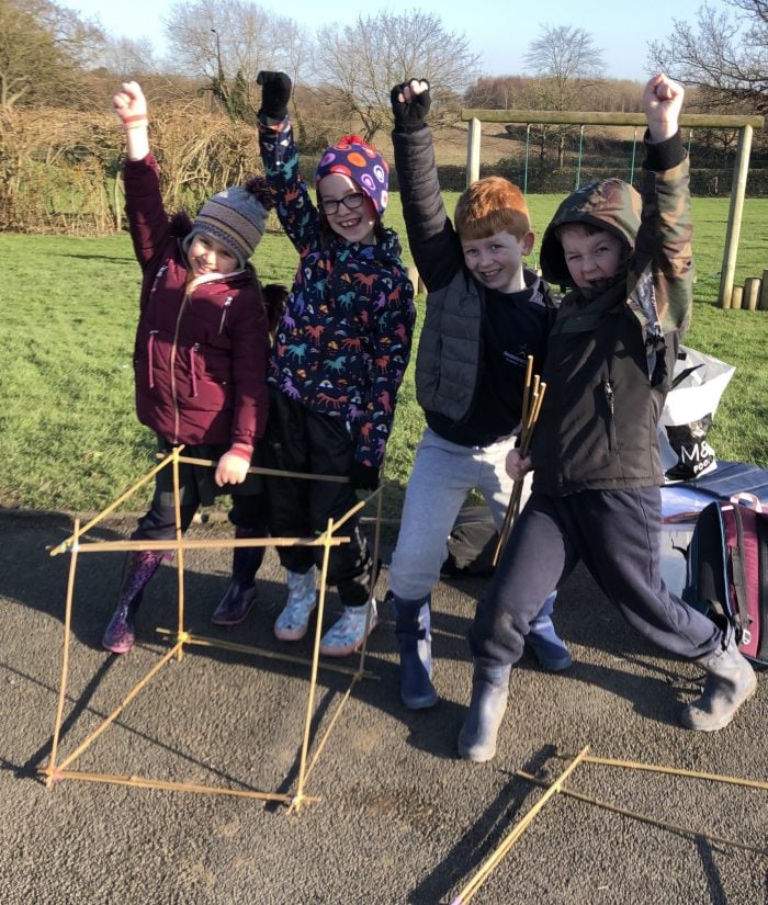 4 children cheering with a cube they made out of bamboo canes during a castles workshop