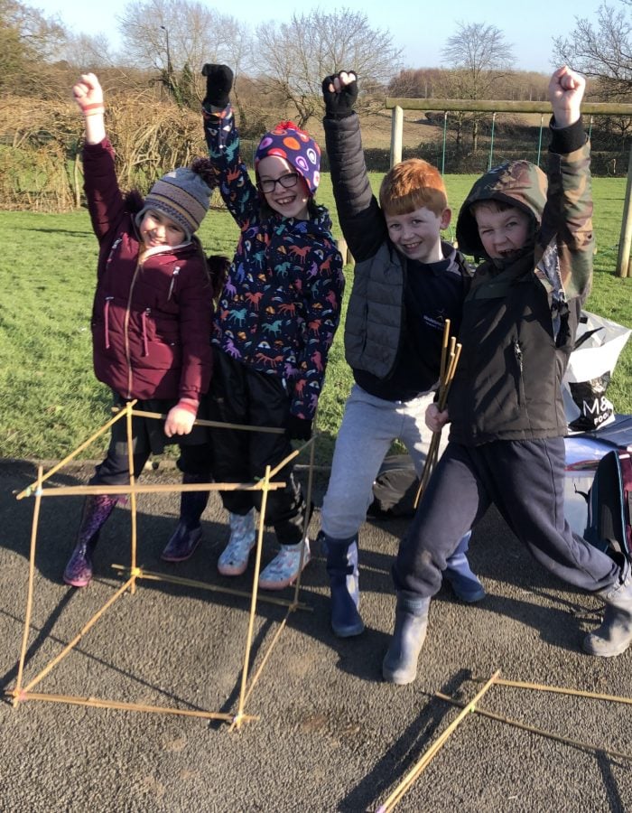4 children cheering with a cube they made out of bamboo canes during a castles workshop