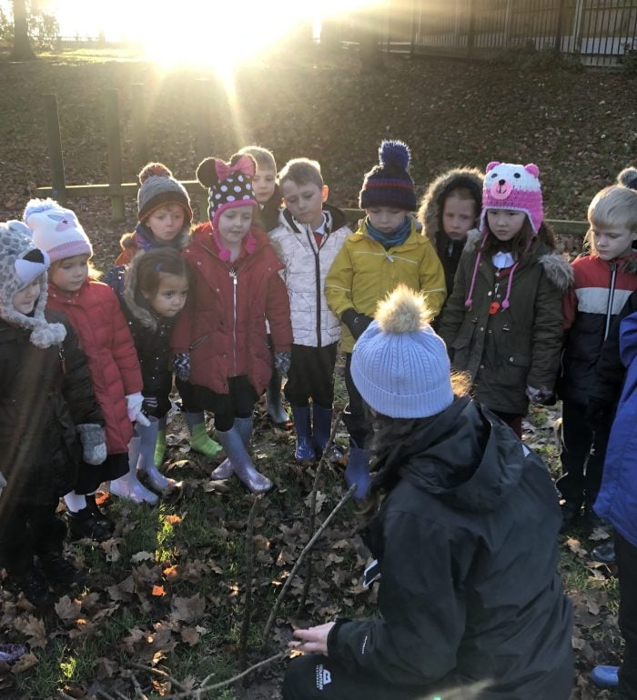 A staff member leading an outdoor workshop, a group of children listening closely