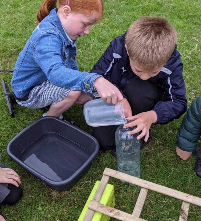 Two children using a jug and water to fill their water rocket with fuel