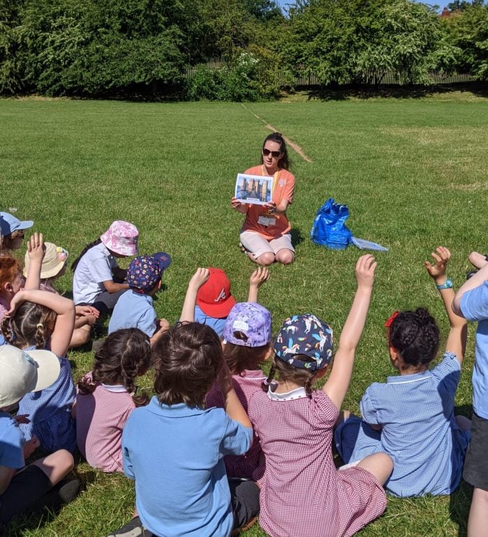 A woman leading a castles workshop in front of a class of children on the grass