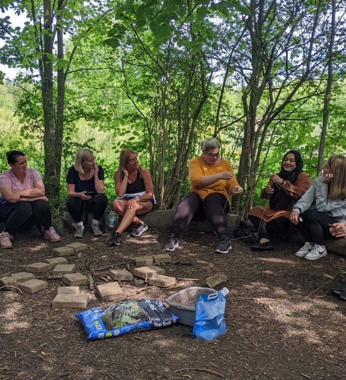 Outdoor learning training being delivered to people sat on logs under trees