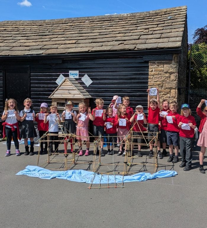 A group of children holding up flags next to a bamboo castle they've constructed