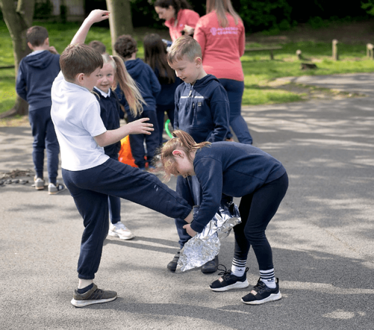 a child almost falling over as another child wraps tin foil around their foot for an experiment